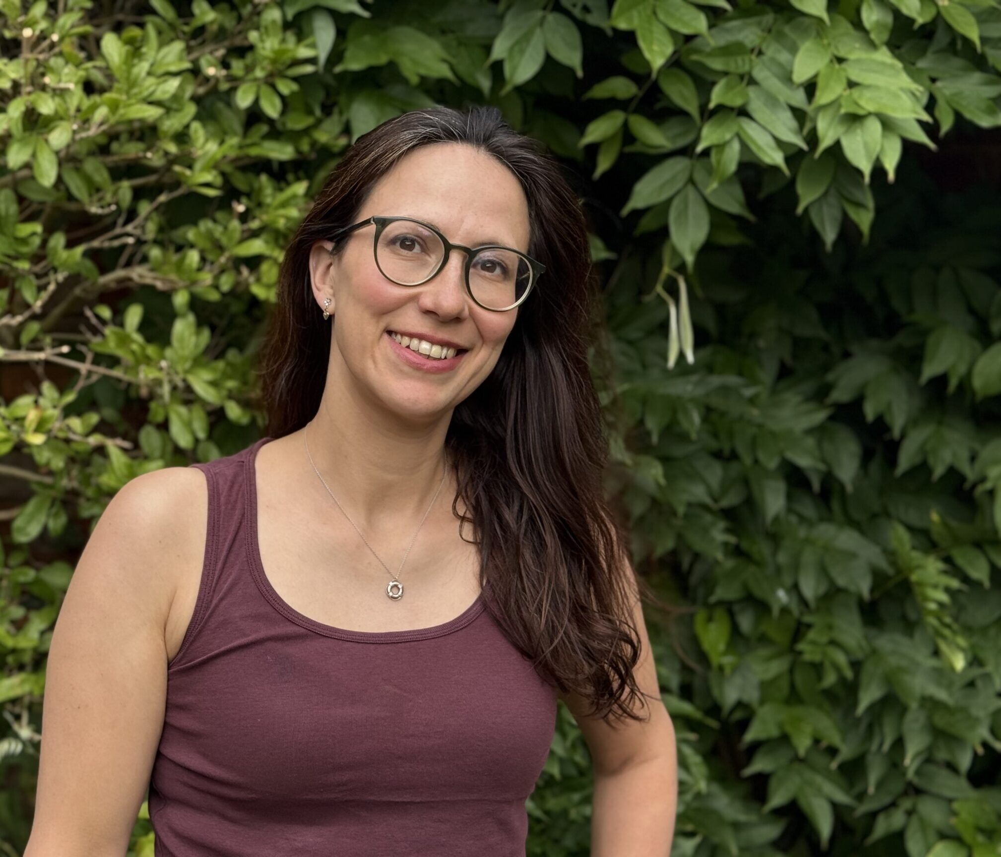 Georgina smiling towards the camera and standing in front of greenery.