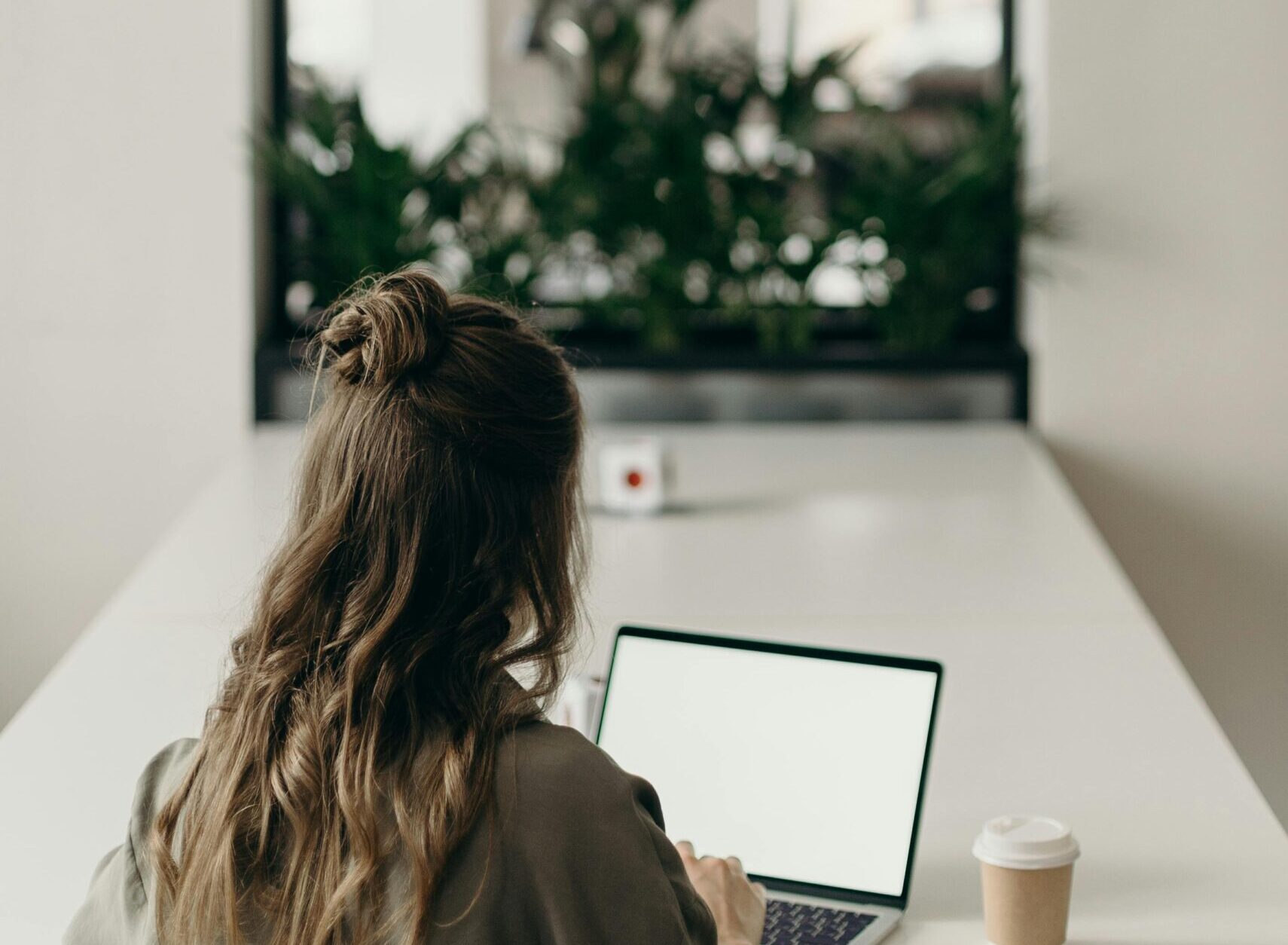 A lady with long hair working on a laptop at a desk with a coffee cup next to her.