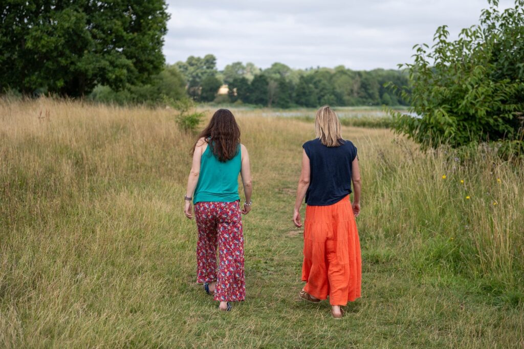 Two women walking away from the camera through a grass meadow side by side