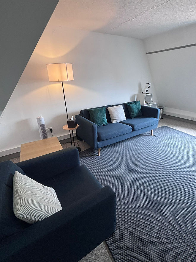 A comfortable chair and sofa either side of a room with soft lighting.