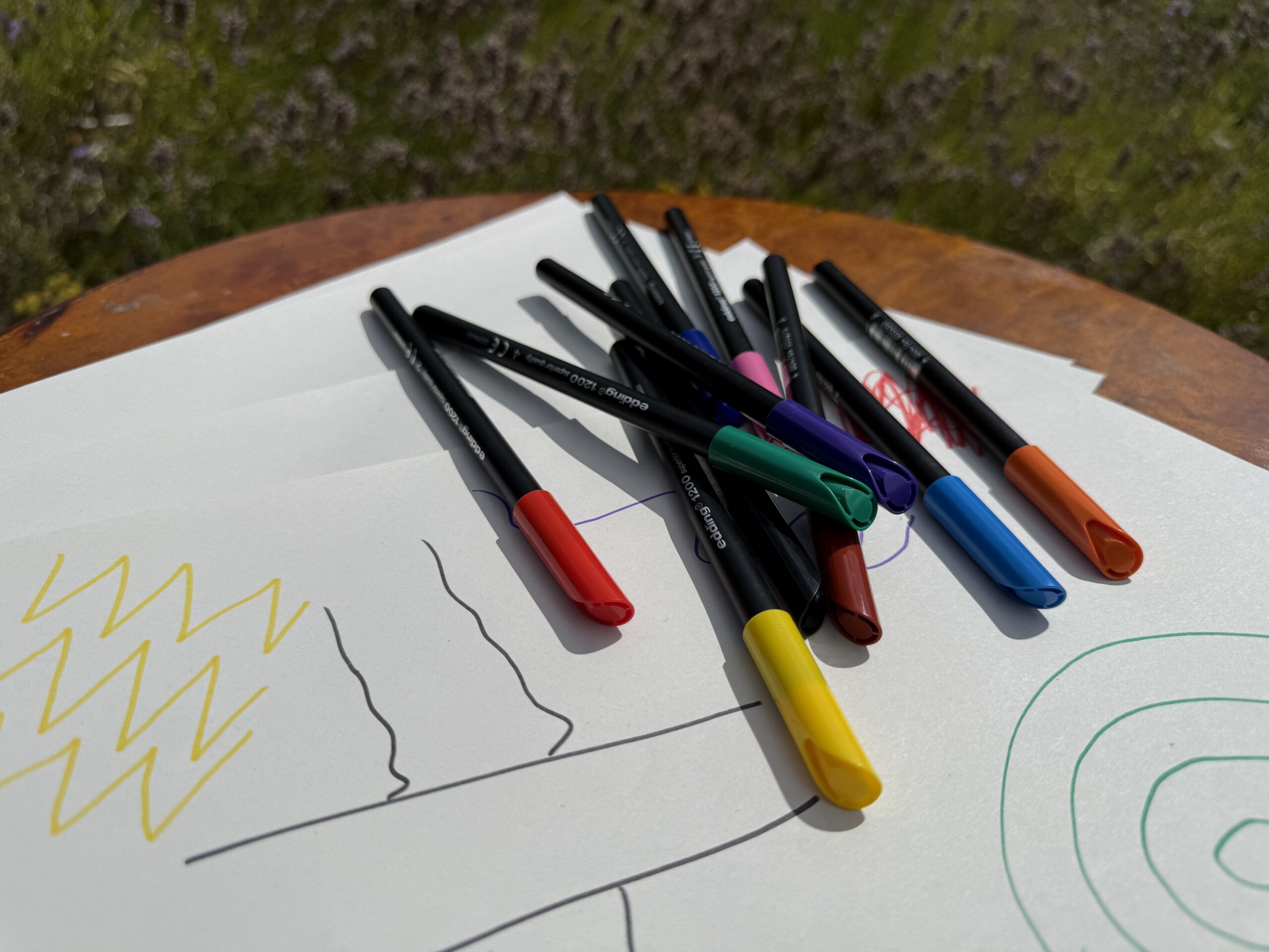 A selection of coloured pens sat on top of some sheets of white paper with drawings and doodles on.